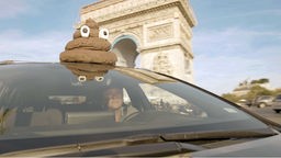 "Holy Shit". Der Regisseur Rubén Abruña fährt mit einem Shit-Emoji auf dem Auto vor dem Arc de Triomphe vorbei.