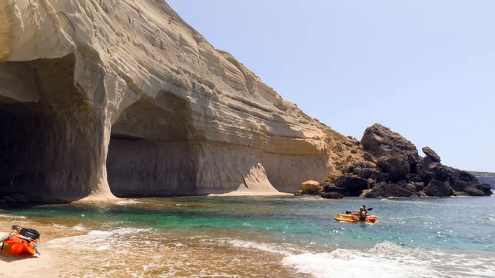 Zwei Kajakfahrer paddeln auf eine große Höhle in einer Steilküste zu