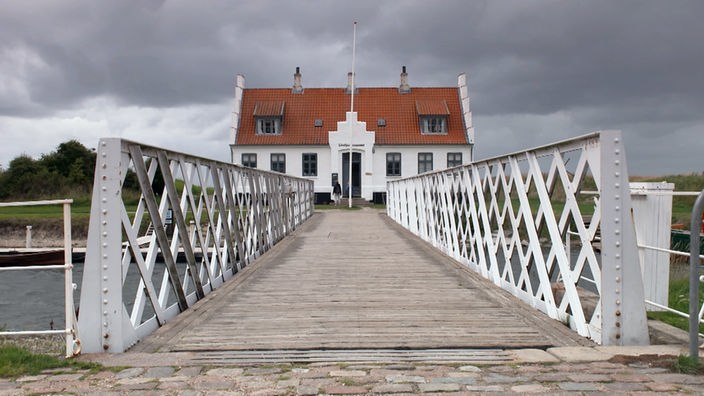 Blick über eine Holzbrücke mit Geländer auf ein historisches Museumsgebäude