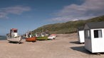 Kleine, weiße Holzhäuser und mehrere Fischerboote auf einem Sandstrand