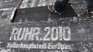 Verschneiter schwarzer Teppich mit Schriftzug Ruhr 2010 Kulturhauptstadt Europas, Fuß Schneeschieber