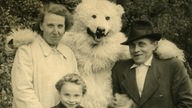 Ein als Eisbär verkleideter Mensch hat den Arm um eine Frau und einen Mann gelegt. Vor ihm stehen zwei Kinder.
