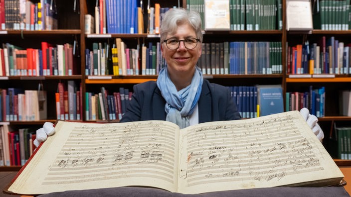 Martina Rebmann, Leiterin der Musikabteilung mit Mendelssohn-Archiv in der Staatsbibliothek zu Berlin, hält die aufgeschlagene ·Handschrift der Sinfonie Nr. 9 des Komponisten L. van Beethoven· in den Händen.
