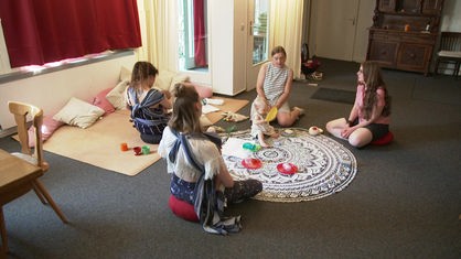 Vier Frauen und ein Baby sitzen im Kreis auf Teppichboden und sprechen miteinander