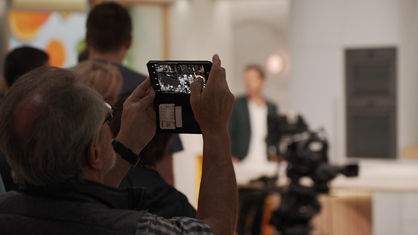 Ein Mann fotografiert ein Fernsehstudio mit der Handykamera.