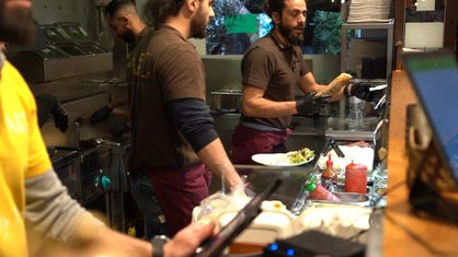 Mehrere Männer hinter einer Imbiss-Theke, die Shawarma zubereiten