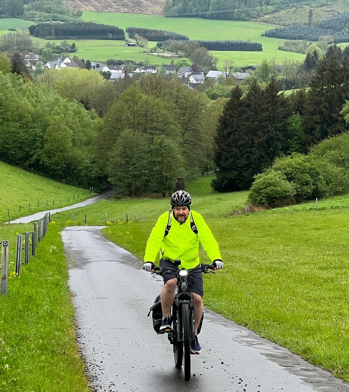 Ein Fahrradfahrer fährt einen Weg, der durch grüne Wiesen führt.