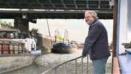 Ein Mann steht an der Reling eines Schiffs, das unter einer Brücke durchfährt