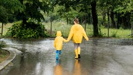 Ein kleines Kind und eine junge Frau laufen Hand in Hand mit Regenmänteln durch den Regen