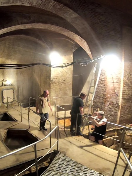 Das Bild zeigt ein beleuchtetes Kellergewölbe mit mehreren Becken, in denen das Aachener Thermalwasser aus der Erde kommt