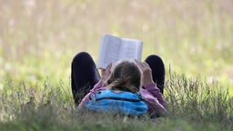 Auf einer Wiese in dem Potsdamer Stadtteil Sacrow, liegt eine Frau im Gras und liest ein Buch,