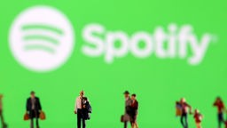 Kleine Figuren stehen vor einem beleuchteten Spotify-Banner.