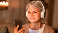 Eine ältere Frau mit Kopfhörern hört Musik.