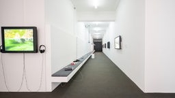 Düsseldorf, 10.9.2023. Ausstellungsraum mit Videoinstallation auf einem Monitor und langer Flur mit ausgelegten Büchern.