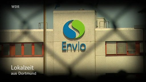 Firmengebäude mit ENVIO-Logo durch Maschendrahtzaun