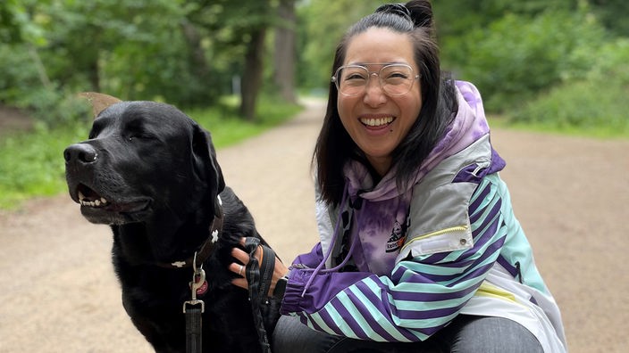 Shia Su im Park mit einem mittelgroßen schwarzen Hund.