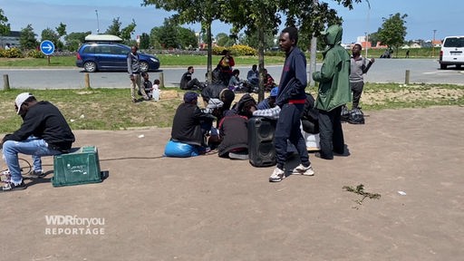 Geflüchtete sitzen im Kreis in einer Straße in Calais