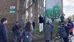Menschen betrachten und fotografieren die Straßenkunst an einer Hauswand in der Hornsey Road in London. Das Werk wird dem Straßenkünstler Banksy zugeschrieben