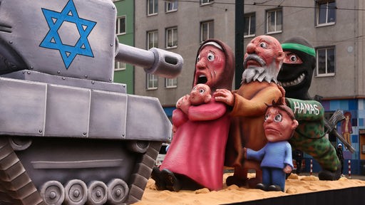 Eine Figurengruppe einer palestinänsischen Familie wird von einer Hamas-Figur vor einen israelischen Panzer gedrängt - Rosenmontagszug in Düsseldorf