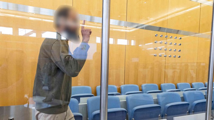 Mutmaßlicher Terrorist von Duismurg betritt mit erhobenem zeigefinger den Gerichtssaal
