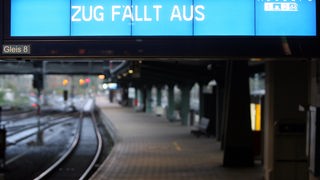 "Zug fällt aus" steht auf der Anzeigetafel am Bahnhof im Hintergrund ein leeres Gleis