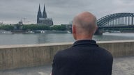 George Menne steht an den Rhein-Terrassen. Im Hintergrund sieht man den Kölner Dom.