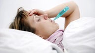 Eine Frau liegt mit einem Fieber-Thermometer im Bett.