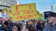 Menschen mit bunten Plakaten demonstrieren vor dem Landtag in Düsseldorf, auf einem steht unter einem Batteriesymbol: "Wir sind am Limit".