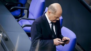Bundeskanzler Scholz schaut vor einer Debatte im Bundestag auf sein Smartphone.