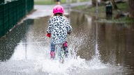Kind fährt durch große Regenpfütze