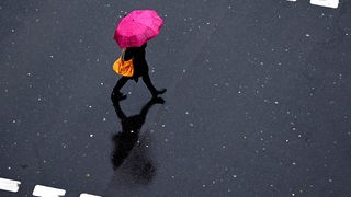 Frau geht mit Regenschirm über die Straße