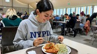 Studentin sitzt in der Mensa am Tisch vor einem Teller mit Essen.