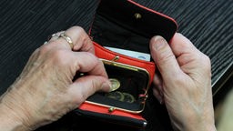 Die Hände einer älteren Dame greifen in ein rotes Portmonnaie, in dem sich Ein-Euro-Münzen und ein Geldschein befinden.