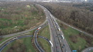 Das Autobahnkreuz Köln-Süd aus der Vogelperspektive, die Autobahn verläuft mehrspurig in den Horizont an dem sich weiter entfernt die Stadt Köln andeutet. Rundherum stehen viele Bäume.
