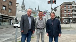 Drei Männer vor Straßenkreuzung, im Hintegrund Aachener Dom