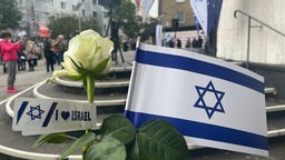 Blumen und ein Zettel mit Herz und der Aufschrift "Israel" neben der Flagge Israels