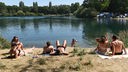 Menschen in Badekleidung sitzen am Ufer eines Sees in der Sonne.
