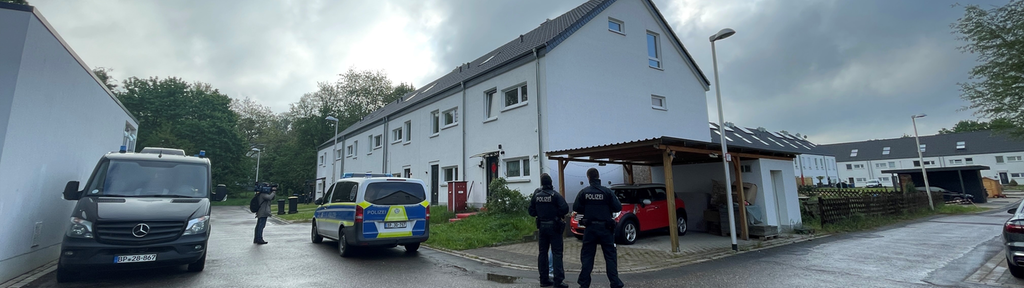 Polizisten und ein Polizeiauto stehen vor einem Wohnhaus