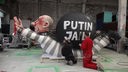 Eine große Putin-Figur in Sträflingskleidung wird von zwei davor knienden Personen bemalt