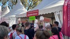 Eine Menschenmenge drängelt sich vor einem Pavillon, in welchem die Teilnehmermedaillen des Kölner Marathons graviert werden.
