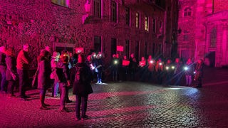 Mehrere Menschen mit Lichtern und Protestplakaten im nächtlichen Domhof