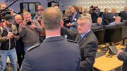 NRW-Innenminister Reul redet mit einem Mann, im Hintergrund stehen mehrere Fotografen