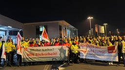 Viele Mitarbeiter mit gelben Westen hinter zwei großen Bannern, im gelben Laternenlicht