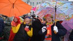 Zu sehen sind zwei Frauen, die sich bunt verkleidet haben und mit jeweils einem Schirm für die Kamera posieren.
