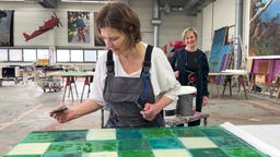 Kulissenmalerin Ewa Klausmann bemalt eine Leinwand mit grüner Farbe und glänzender Lasur