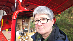 Schwester Ursula steht vor einem roten Rollermobil, mit dem die Pfarrei St. Johann in Duisburg unterwegs ist.