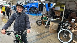 Ein Junge mit Fahrradhelm auf einem Fahrrad, im Hintergrund ein Stand mit E-Bikes