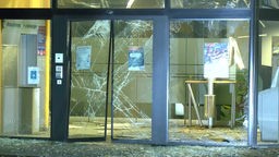 Die Glasfront einer Bankfiliale ist zerstört. Auf dem Gehweg liegen Splitter. Im Foyer der Bank liegen Teile des Geldautomaten.