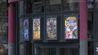 Auf dem Bild sind Kino-Plakate zu sehen, die neben dem Kino-Eingang hängen.