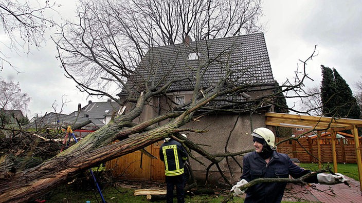 Feuerwehrmänner tragen Äste eines auf ein Haus gestürzten Baumes weg
